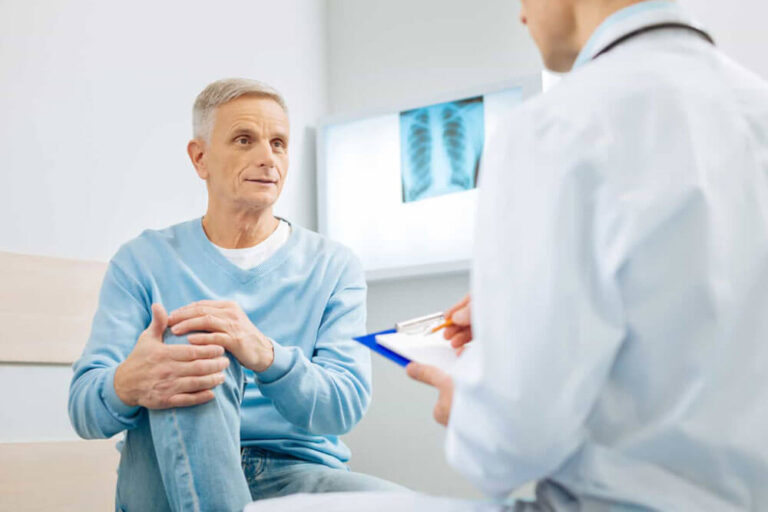 Good looking nice aged man holding his knee and looking at his doctor