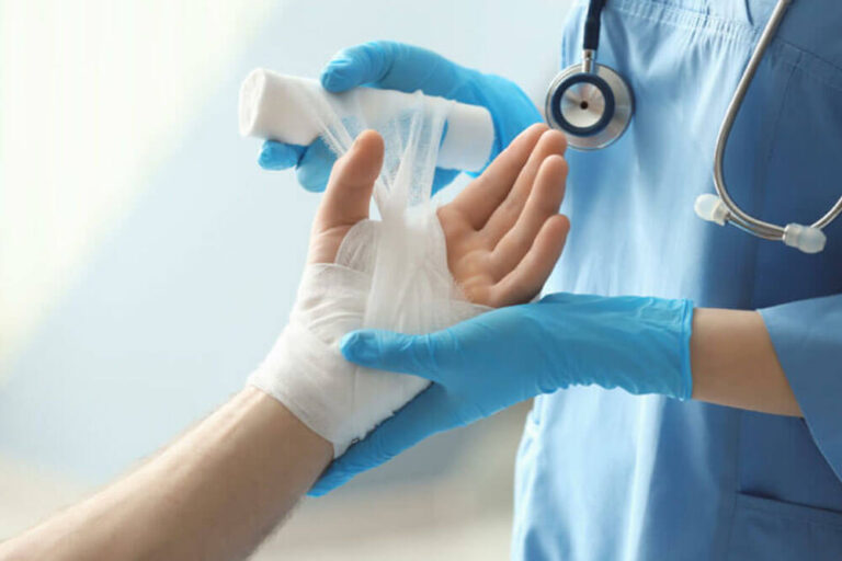 Medical assistant applying bandage onto patient's hand in clinic