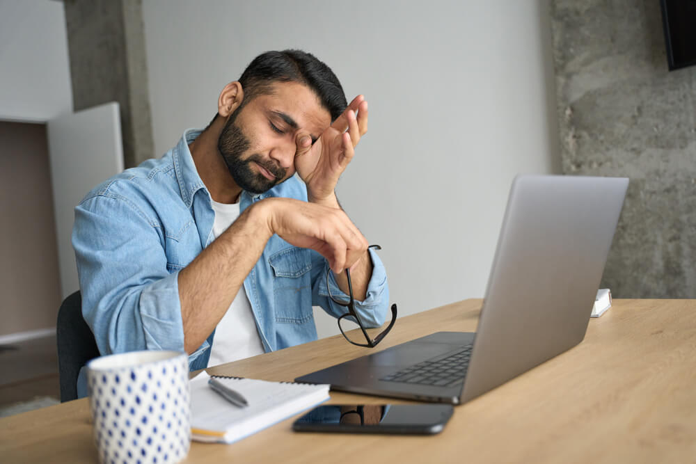 Exhausted man rubbing eyes sitting in home