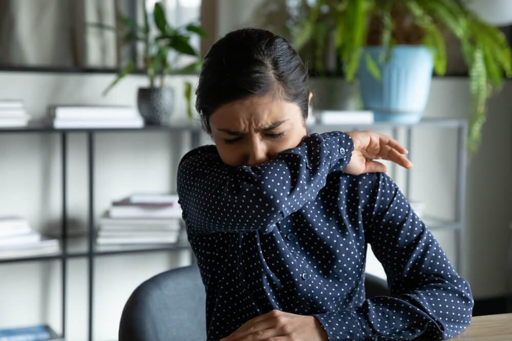 Girl sitting in office, coughing in elbow,