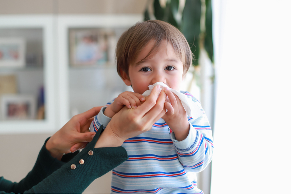 Baby boy blowing nose into tissue pape