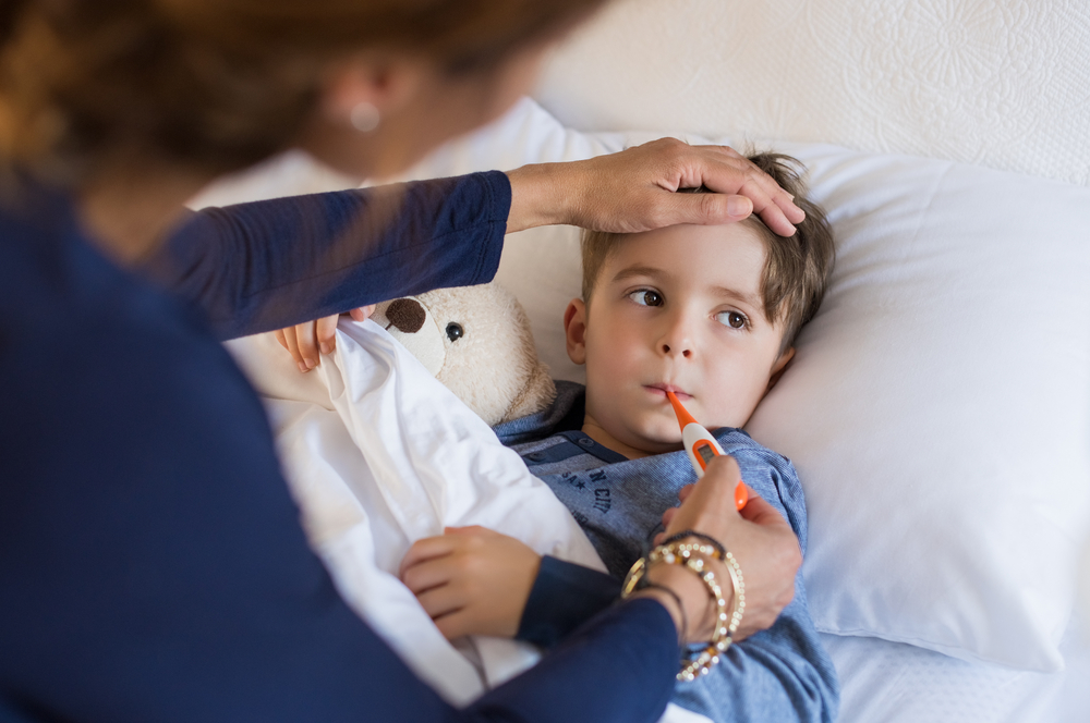 Sick boy with thermometer laying in bed and mother hand